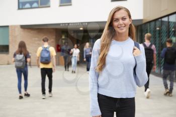 Portrait Of Smiling Female High School Student Outside College Building With Other Teenage Students In Background