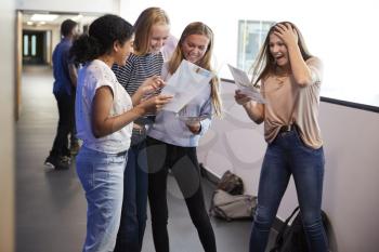 Excited Female Teenage High School Students Celebrating Exam Results In School Corridor