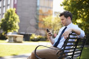 Businessman Outdoors Using Mobile Phone On Lunch Break In Park
