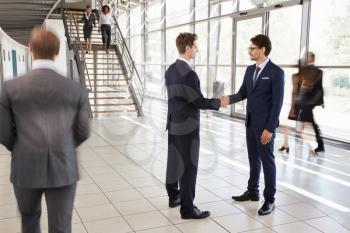 Two white businessmen shaking hands in a busy modern lobby
