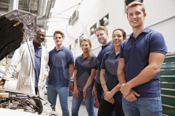 Car mechanic and apprentices in a garage looking to camera
