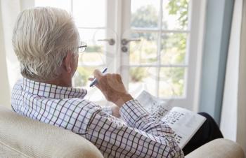 Senior man sitting in an armchair doing  crossword, close up