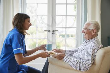 Nurse serving a cup of tea to a senior man at home, close up
