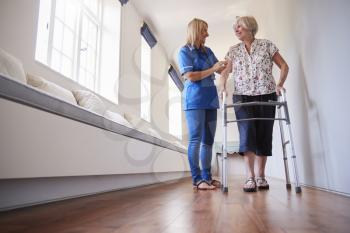 Nurse helping senior woman use a walking frame, full length
