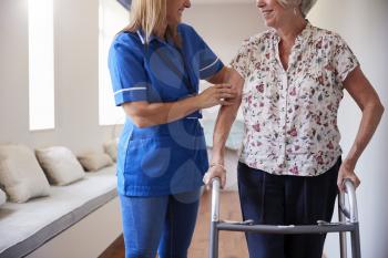 Nurse helping senior woman use a walking frame, mid section