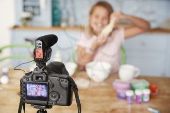Young girl video blogging in kitchen seen through camera