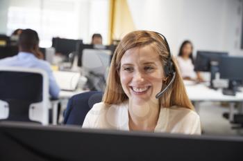 Young woman working at computer with headset in busy office