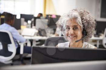 Middle aged woman working at computer with headset in office