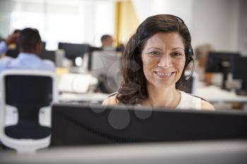 Middle aged woman working at computer with headset in office
