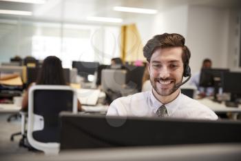 Young man working at computer with headset in busy office