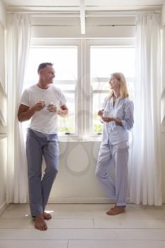 Mature Couple Standing By Bedroom Window With Hot Drink