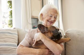 Senior Woman Sitting On Sofa At Home With Pet French Bulldog