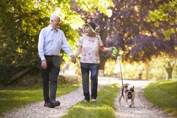 Senior Couple Walking With Pet Bulldog In Countryside