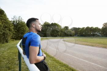 Male athlete wearing earphones taking a break at a track