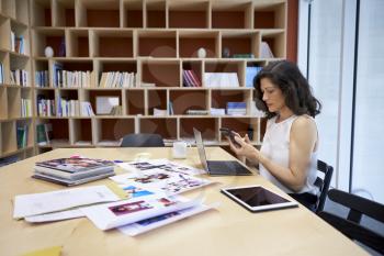 Woman in creative media office using smartphone at her desk