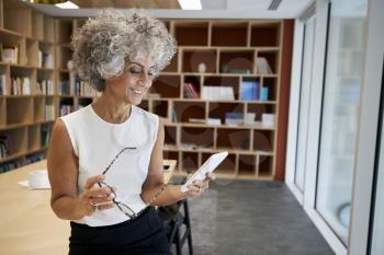 Senior businesswoman holding glasses, using smartphone