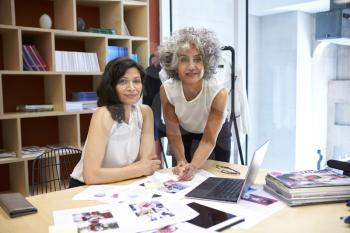 Two female creatives working in office looking to camera