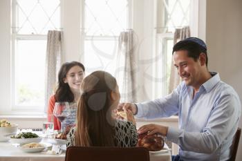 Jewish man sharing challah bread with family at Shabbat meal