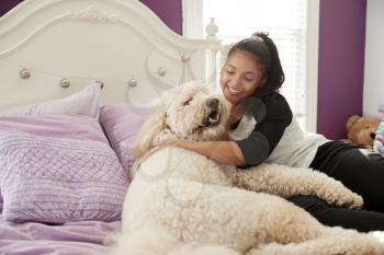Young teen girl cuddling pet dog on her bed