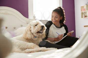 Young teen girl doing homework on her bed with pet dog