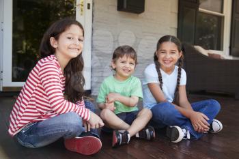 Portrait Of Children Sitting On Porch Of House Together
