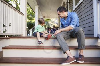 Father And Son Sit On Porch Of House Playing With Toys Together