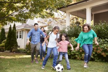 Multi Generation Family Playing Soccer In Garden