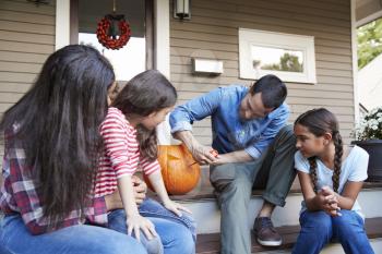 Family Carving Halloween Pumpkin On House Steps