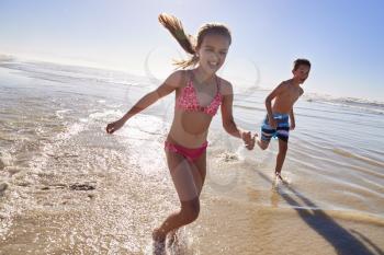 Boy And Girl On Summer Vacation Running Through Waves