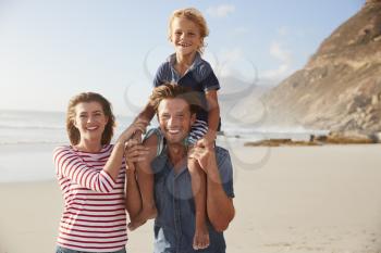 Portrait Of Parents Carrying Son On Shoulders On Beach Vacation