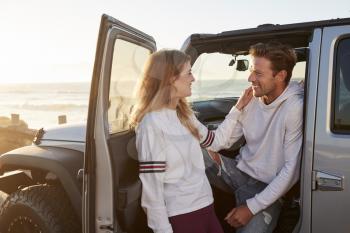 Young couple on road trip looking at each other by their car