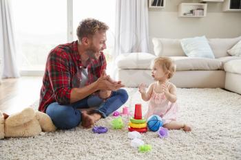 Young father and toddler daughter clapping in sitting room