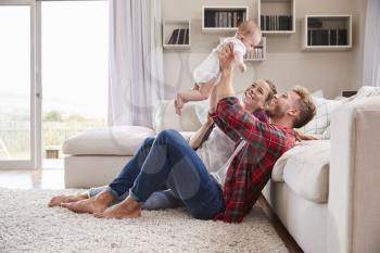 Young white couple play with their toddler in sitting room