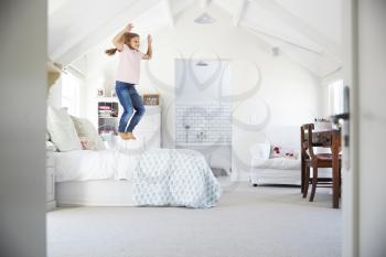 Happy young girl jumping on her bed in her bedroom