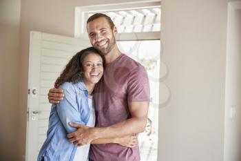 Portrait Of Couple By Open Front Door In Lounge Of New Home