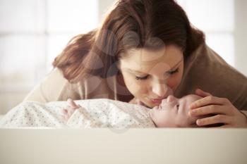 Mother Kissing Newborn Baby Lying On Changing Table In Nursery