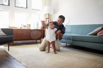 Father Encouraging Baby Daughter To Take First Steps At Home