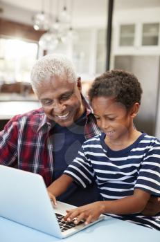 Grandfather And Grandson Sitting Around Table At Home Using Laptop Together