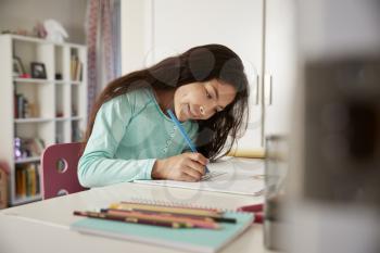 Young Girl Sitting At Desk In Bedroom Doing Homework