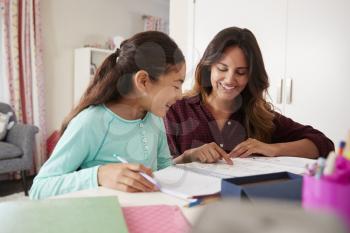 Mother Helping Daughter With Homework Sitting At Desk In Bedroom