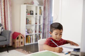 Young Boy Sitting At Desk In Bedroom Doing Homework