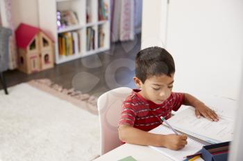 Young Boy Sitting At Desk In Bedroom Doing Homework