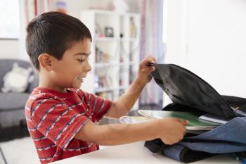 Boy In Bedroom Packing Bag Ready For School