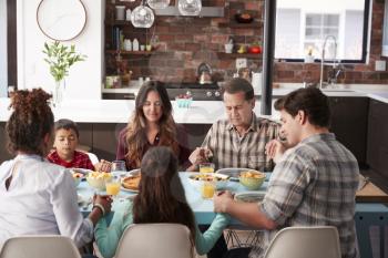 Multi Generation Family Praying Before Meal Around Table At Home