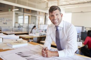 Middle aged male architect smiling to camera in his office