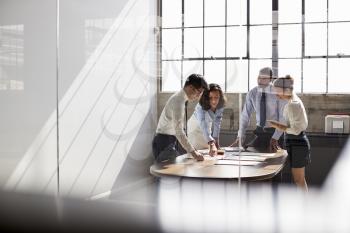 Four business colleagues stand talking in a meeting room