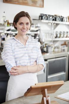 Young smiling woman behind counter at coffee shop, vertical