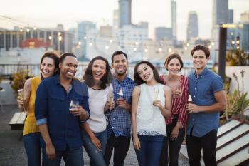 Portrait Of Friends Gathered On Rooftop Terrace For Party With City Skyline In Background Making Toast With Drinks