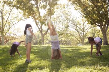 Four young girlfriends doing handstands together in a park