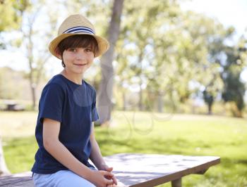 Young schoolboy in hat sits on park bench smiling to camera